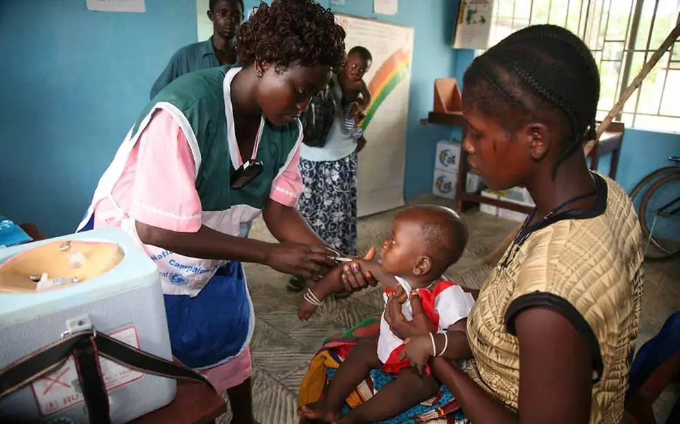 Artikel 24: Gesundheit Sierra Leone: Gesundheitshelferin impft Kind in einer Gesundheitsstation