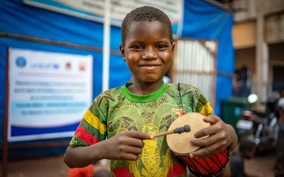 Ein Junge in Mali hält lächelnd eine kleine Trommel in der Hand. | © UNICEF/N’Daou Ein geflüchteter Junge in Mali mit einer Trommel in der Hand.