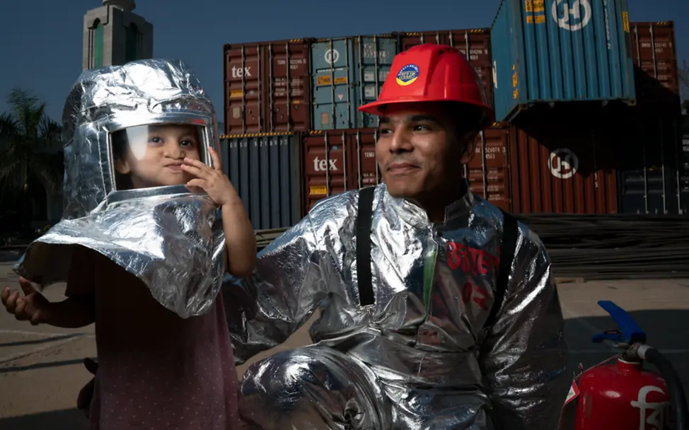 Mohammad Jahirul Islam, 28, und seine Tochter Jisha, 3, in Brandschutzkleidung auf dem Gelände der Fakir Fashion Ltd. | © UNICEF/UN0292175/Sokol Mohammad Jahirul Islam, 28, und seine Tochter Jisha, 3, in Brandschutzkleidung auf dem Gelände der Fakir Fashion Ltd.